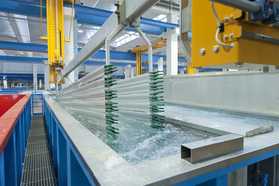 Overhead crane moving aluminum profile racks over anodizing tanks.